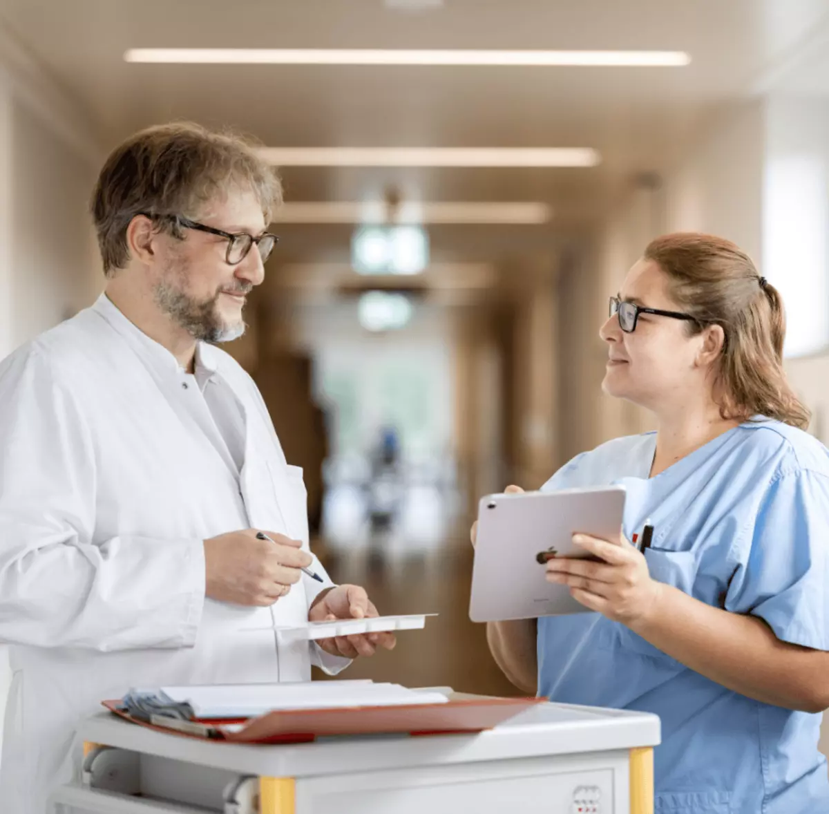Arzt und Mitarbeiterin im Gespräch auf dem Klinikflur – interdisziplinäre Zusammenarbeit im Reha-Alltag.