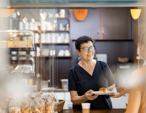 Mitarbeiterin gibt an der Ausgabestation Essen an eine Person aus.