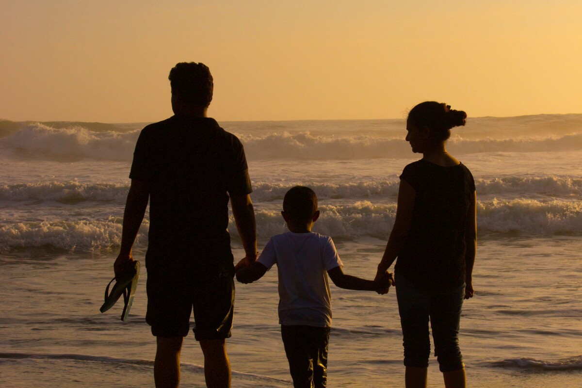 Silhouette einer dreiköpfigen Familie, die im Sonnenuntergang am Strand steht und sich an den Händen hält