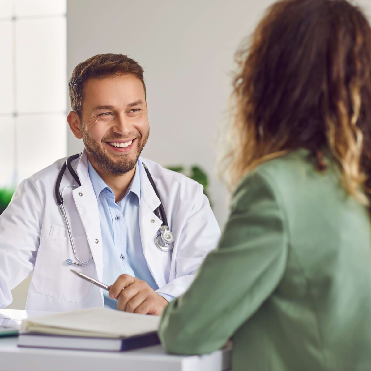 Lachender Arzt berät Patientin im Gespräch – ganzheitlicher Reha-Ansatz mit medizinischer und psychosozialer Unterstützung.